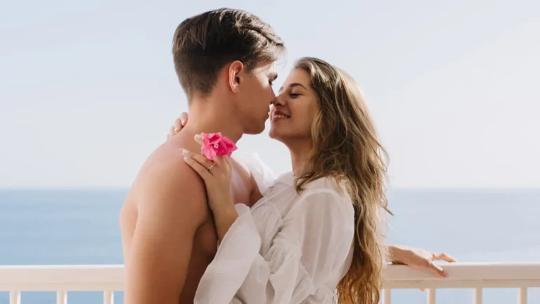 Couple hugging on a balcony with the ocean in the background, romantic seaside moment.
