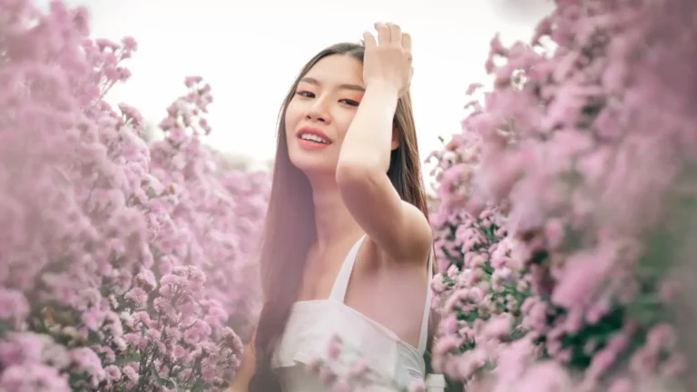 Aesthetic photo of a stunning young woman with dark hair and brown eyes wearing a white dress, smiling gracefully in a purple lavender field.