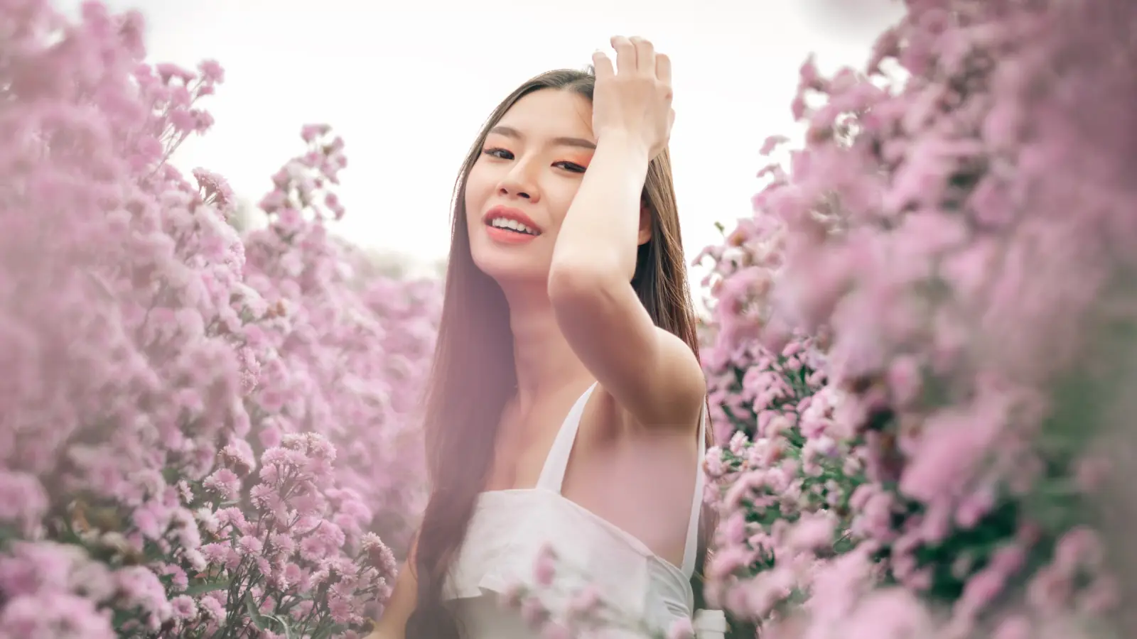 Aesthetic photo of a stunning young woman with dark hair and brown eyes wearing a white dress, smiling gracefully in a purple lavender field.