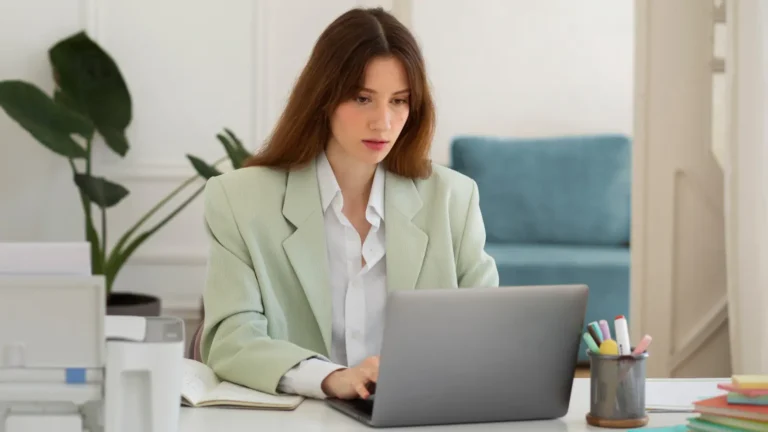 Focused brunette woman sitting at a desk working on her laptop in a cozy, modern workspace, illustrating productivity and remote work