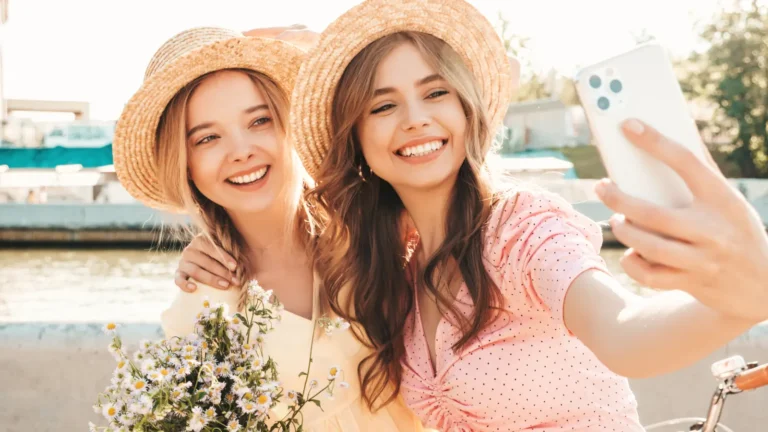 Two women laughing and smiling together, enjoying a joyful moment and friendship in a bright outdoor setting