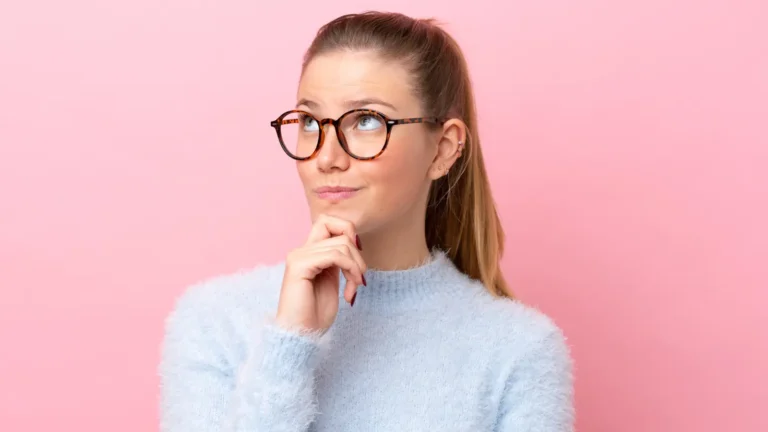 Portrait of a beautiful young woman wearing glasses, looking thoughtful and focused, showing intelligence and elegance in a soft natural light.